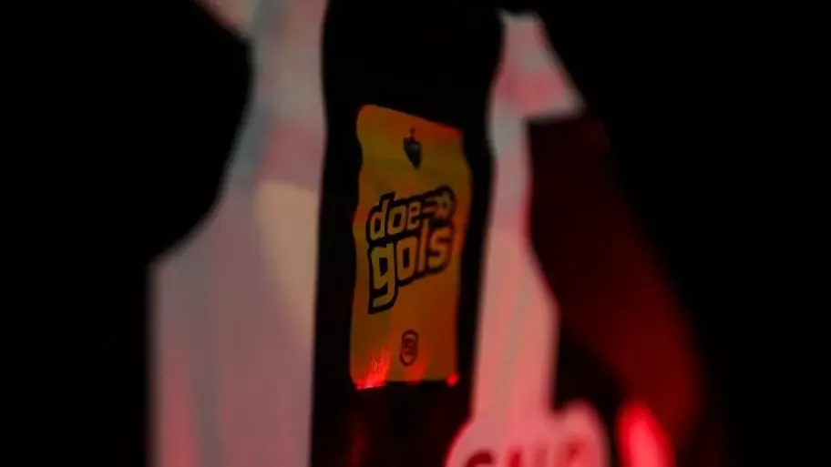 Patch do Doe Gols em uniforme de atleta, iluminado por luz vermelha em ambiente noturno.