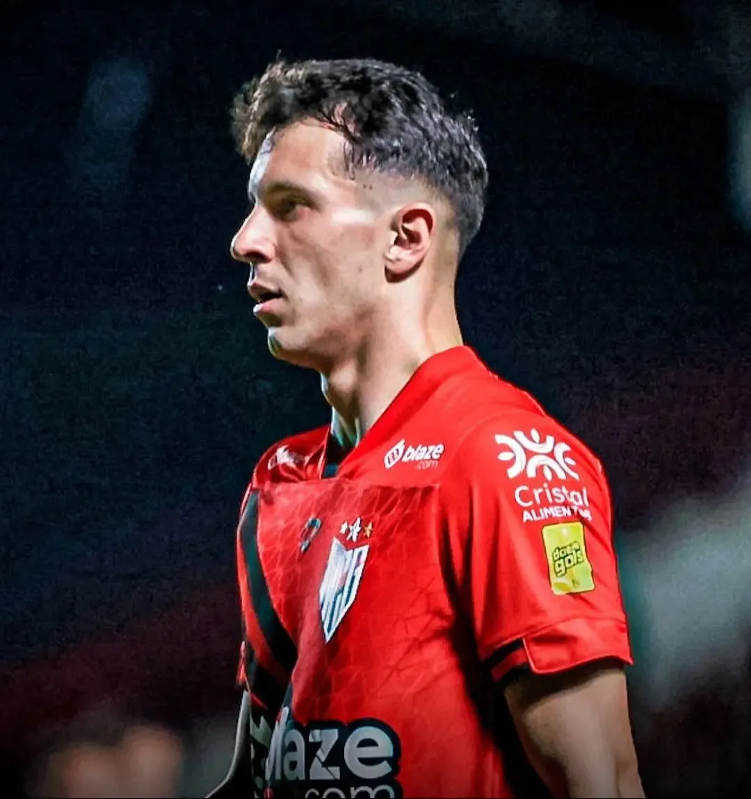 Jogador do Atlético-GO em campo com a camisa vermelha exibindo o patch do Doe Gols na manga, durante partida noturna no Castelo do Dragão.